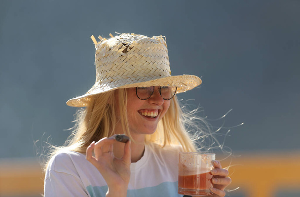 Une jeune femme avec un cigare et une tasse de boisson. Une fille avec un chapeau de beurre. - Photo, image