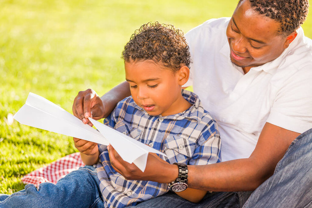 Feliz padre afroamericano e hijo de raza mixta jugando con aviones de papel en el parque. - Foto, imagen