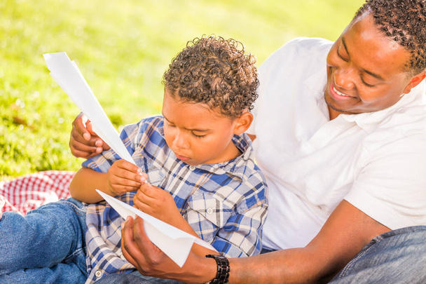 Felice padre afroamericano e figlio di razza mista che gioca con aerei di carta nel parco. - Foto, immagini