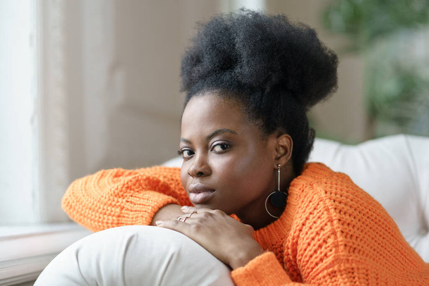 Trendige afrikanische Millennial-Frau in lässiger Kleidung und lockigem Haar liegt auf der Couch und entspannt zu Hause - Foto, Bild