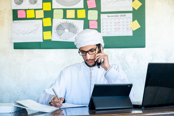 arabialainen mies käyttää matkapuhelintaan työskennellessään viestintätarkoituksiin - Valokuva, kuva