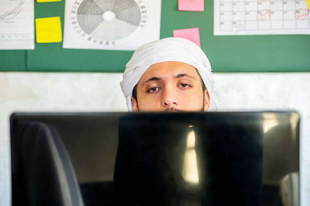 El joven árabe está ocupado con su trabajo desde su casa con alta concentración usando su computadora portátil con tablero pegajoso en su oficina - Foto, imagen