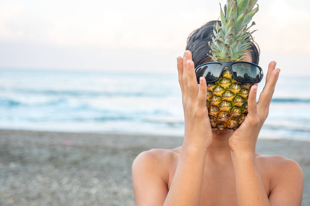 Young boy holding pineapple near the sea - Zdjęcie, obraz