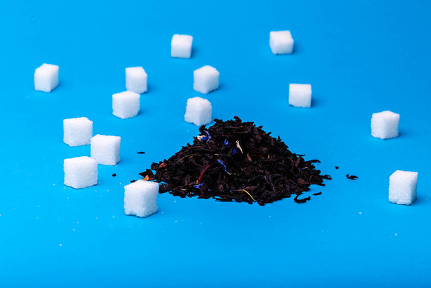 Куча черного чая и кубики белого сахара на синем фоне - Фото, изображение