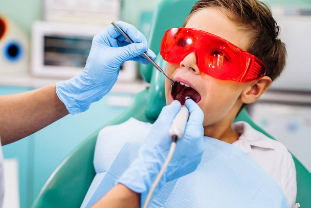 Patient mit offenem Mund in Zahnklinik. Vorbereitung auf zahnärztliche Behandlung. Verwendung von Watte, um Speichel, Bohrmaschine, Zahnspiegel, Pinzette und andere Geräte zu sammeln. Rechtzeitige Behandlung ist wichtig. - Foto, Bild