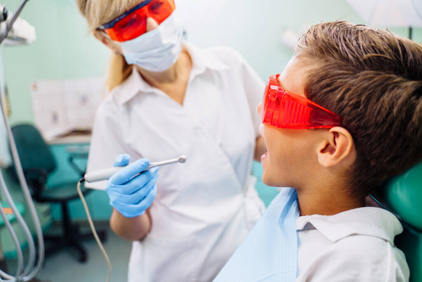 Zahnärztliche Untersuchung wird Schöner Mann umgeben von Zahnarzt und seine Assistentin gegeben. Zahnärztin in der Zahnarztpraxis spricht mit der Patientin und bereitet sich auf die Behandlung vor. - Foto, Bild