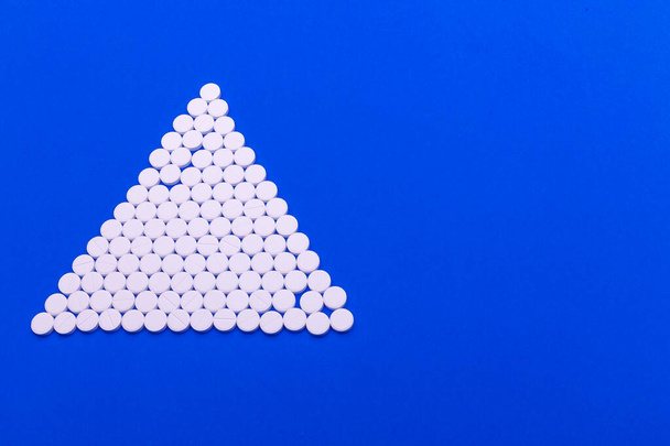 Κοντινό πλάνο πυραμίδα έννοια των λευκών χαπιών σε μπλε φόντο με αντίγραφο χώρο. Εστίαση σε πρώτο πλάνο, μαλακό bokeh. - Φωτογραφία, εικόνα