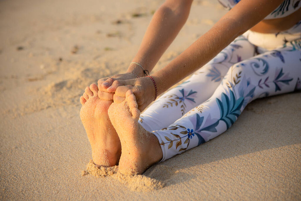 Gros plan des pieds féminins. Femme assise sur le sable, pratiquant le yoga. Paschimottanasana, position coudée vers l'avant assise. Les mains tenant de gros orteils. Concept de yoga extérieur. Ça marche. Plage de Thomas, Bali - Photo, image