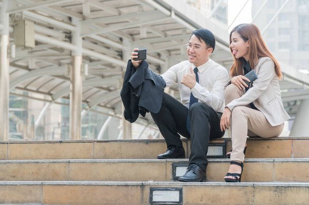 Kaksi liikemiestä istuu portaissa ja ottaa itse eli älypuhelin kädessä moderni kaupunki. - Valokuva, kuva
