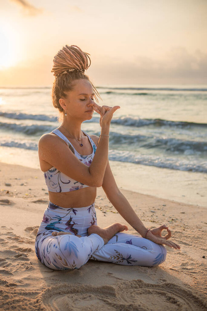 Mujer yogui sentada en pose de loto, practicando Anuloma Viloma Pranayama, respiración nasal alterna. Control prana, control de la respiración. Ejercicio respiratorio. Hora del atardecer. Retiro de yoga. Playa de Thomas, Bali - Foto, Imagen