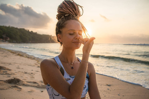 Yogi woman practicing Nadi Shodhana Pranayama, Alternate Nostril Breathing. Control prana, control of breath. Breathing exercise. Self care concept. Sunset time. Yoga retreat. Thomas beach, Bali - Foto, imagen