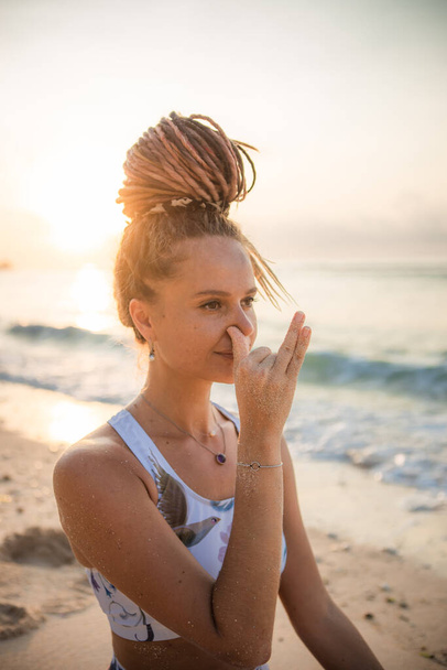 Yogi woman practicing Nadi Shodhana Pranayama, Alternate Nostril Breathing. Control prana, control of breath. Breathing exercise. Self care concept. Sunset time. Yoga retreat. Thomas beach, Bali - Φωτογραφία, εικόνα