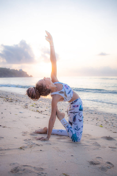 Outdoor yoga op het strand. Jonge vrouw oefenen variatie van Ushtrasana, Camel Pose, knielen terug buigen van asana. Flexibele wervelkolom. Yoga retraite. Zelfzorgconcept. Zonsondergang tijd. Strand van Thomas, Bali - Foto, afbeelding