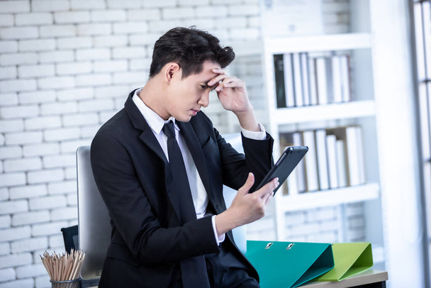Stressed businessman worked with a tablet and having a headache after business losses In the office room background. - Foto, imagen