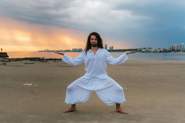 Stock photo of adult man with long hair doing yoga poses in the beach. - Foto, Imagen