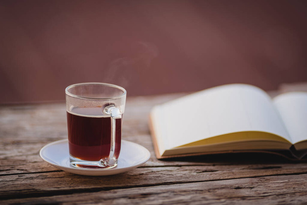 Egy csésze forró reggeli kávé egy fából készült asztalon, egy naplójegyzettel a hálószoba erkélyén, hogy üdvözölje a reggeli napsütést, egy pohár fekete kávé, jegyzetfüzettel a fa asztalon. - Fotó, kép