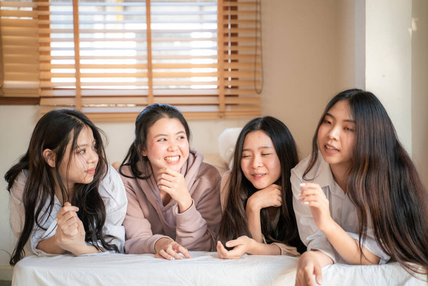 ベッドの上に寝そべっている美しいアジアの女性のグループが笑いながら、屋内で会う楽しむ居心地の良いベッドのファッショナブルなモデルについて話します - 写真・画像