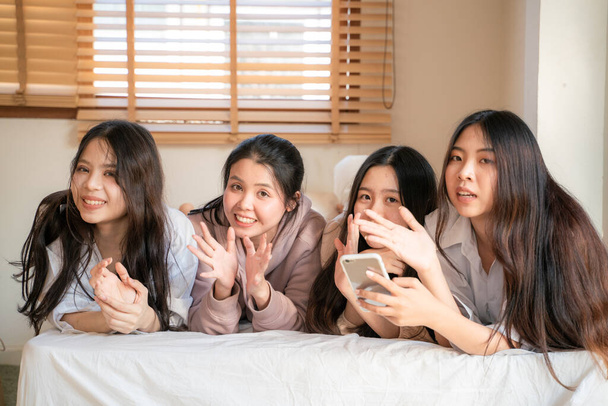Grupa pięknych azjatyckich kobiet leżących na łóżku śmiejących się i rozmawiających razem na przytulnym łóżku modne modelki cieszące się spotkaniem wewnątrz - Zdjęcie, obraz