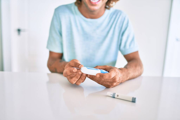 Молодий іспаномовний діабетик чоловік посміхається щасливим вимірюванням рівня глюкози в домашніх умовах
 - Фото, зображення