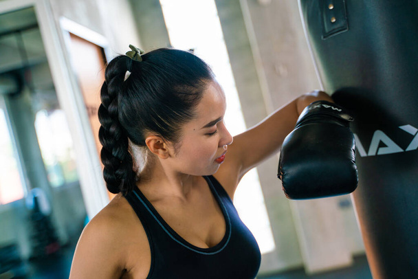 Vonzó ázsiai nő üt egy fekete táska boxkesztyűvel a tornateremben, Kickbox - Fotó, kép