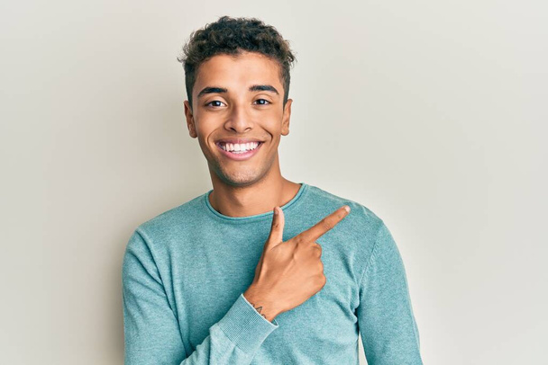 Jonge knappe Afro-Amerikaanse man draagt casual kleding lachend vrolijk wijzend met hand en vinger naar de zijkant  - Foto, afbeelding