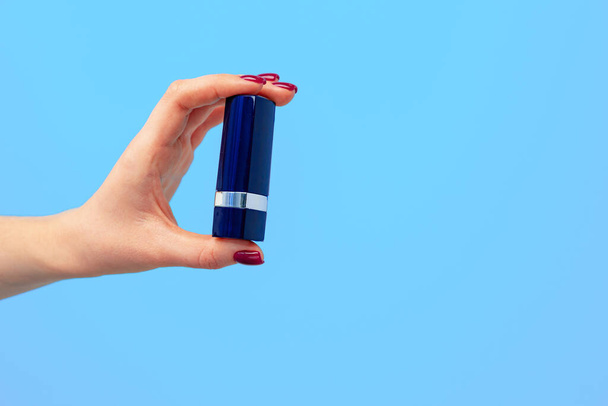 Female hand holding lipstick against blue background - Photo, image