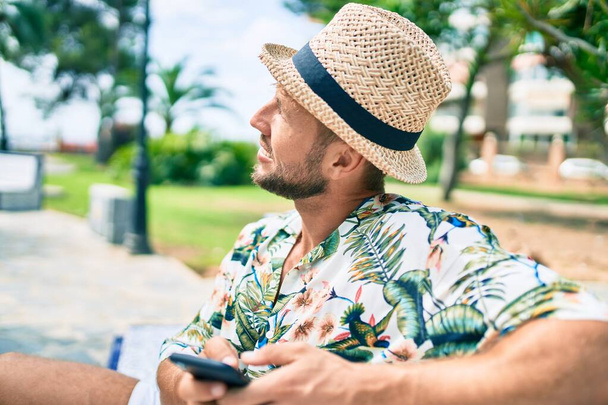 Caucásico guapo hombre sonriendo feliz al aire libre utilizando el teléfono inteligente - Foto, imagen