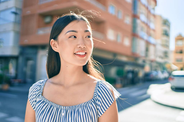 Νεαρή Κινέζα γυναίκα χαμογελά ευτυχισμένη περπατώντας στο δρόμο της πόλης. - Φωτογραφία, εικόνα