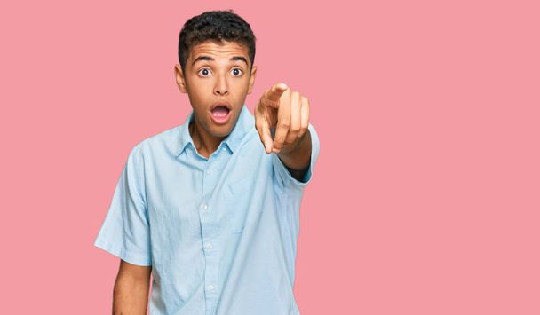 Young handsome african american man wearing casual clothes pointing with finger surprised ahead, open mouth amazed expression, something on the front  - Фото, зображення