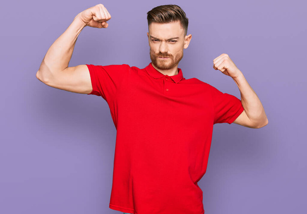 Mladý rusovlasý muž v neformálních šatech ukazuje pyšné svaly na pažích. fitness koncept.  - Fotografie, Obrázek