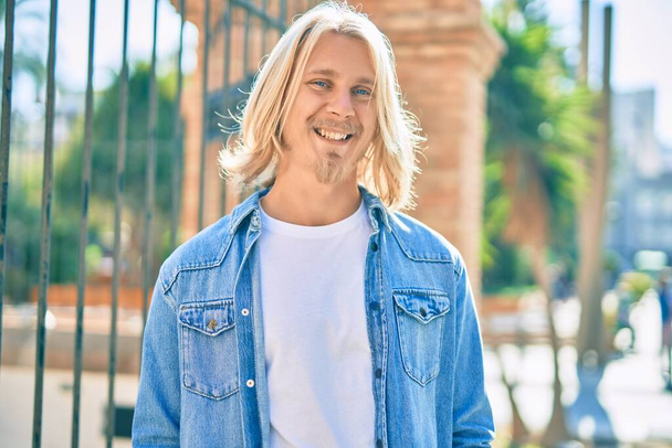 Jeune homme blond scandinave souriant heureux debout à la ville. - Photo, image