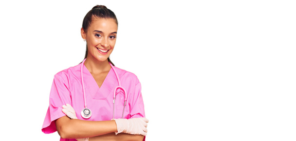 Mujer hispana joven vistiendo uniforme médico y estetoscopio cara feliz sonriendo con los brazos cruzados mirando a la cámara. persona positiva.  - Foto, imagen