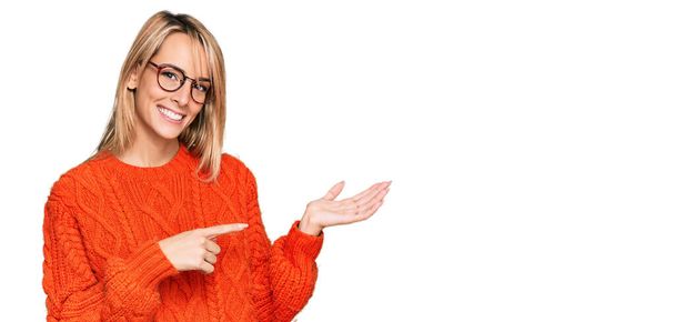 Beautiful blonde woman wearing casual clothes and glasses amazed and smiling to the camera while presenting with hand and pointing with finger.  - Photo, Image