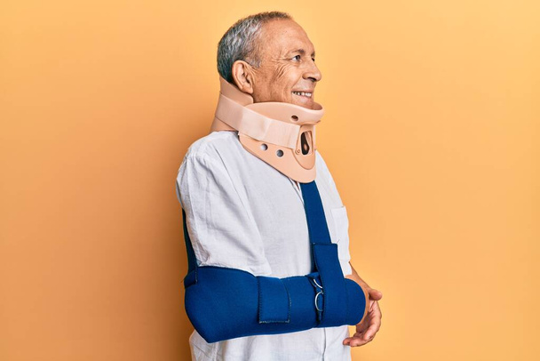 Handsome mature senior man wearing cervical collar and arm on sling looking away to side with smile on face, natural expression. laughing confident.  - Fotografie, Obrázek