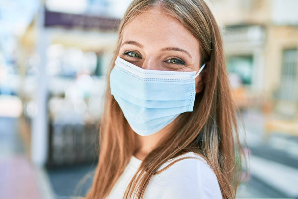 Young caucasian woman wearing coronavirus protection medical mask walking at the city - Fotó, kép