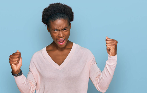 Young african american girl wearing casual clothes angry and mad raising fists frustrated and furious while shouting with anger. rage and aggressive concept.  - 写真・画像