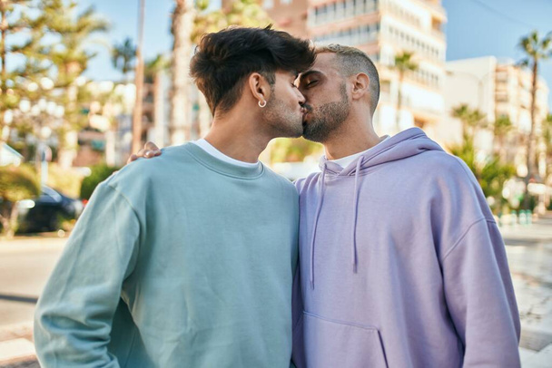 Νεαρό γκέι ζευγάρι αγκαλιάζεται και φιλιέται στην πόλη. - Φωτογραφία, εικόνα