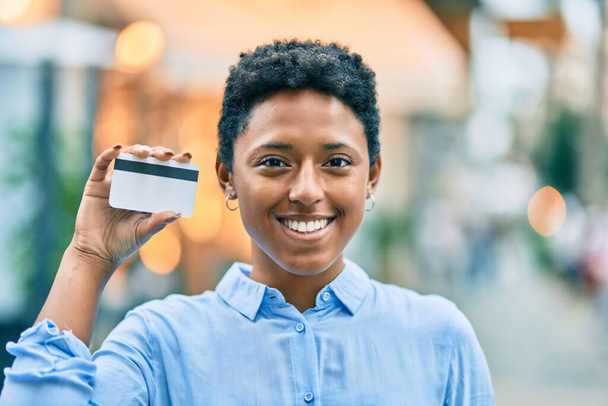 Молода афроамериканська дівчина, яка посміхається, тримаючи кредитну картку в місті.. - Фото, зображення