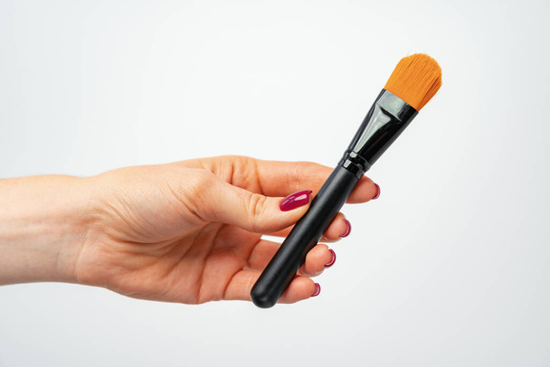 Female hand holding make up brush against gray background - Foto, immagini