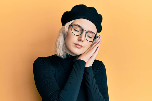 Young blonde girl wearing french look with beret sleeping tired dreaming and posing with hands together while smiling with closed eyes.  - Fotoğraf, Görsel