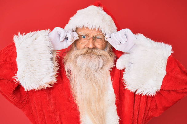 Alter älterer Mann mit grauen Haaren und langem Bart im Weihnachtsmann-Kostüm, mit Brille skeptisch und nervös, die Stirn runzelnd vor Ärger. Negative Person.  - Foto, Bild