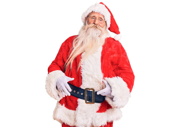 Oude senior man met grijs haar en lange baard in traditionele kerstman kostuum ziet er slaperig en moe, uitgeput voor vermoeidheid en een kater, luie ogen in de ochtend.  - Foto, afbeelding