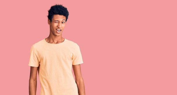 Jeune homme afro-américain portant des vêtements décontractés clin d'oeil en regardant la caméra avec une expression sexy, gai et heureux visage.  - Photo, image