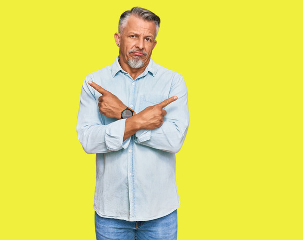 Grauhaariger Mann mittleren Alters in lässiger Kleidung, der mit den Fingern nach beiden Seiten zeigt, unterschiedliche Richtung  - Foto, Bild