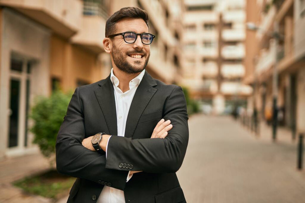 Jeune homme d'affaires hispanique les bras croisés souriant heureux à la ville. - Photo, image