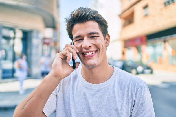 Genç beyaz adam gülümsüyor. Şehirdeki akıllı telefondan konuşuyor.. - Fotoğraf, Görsel
