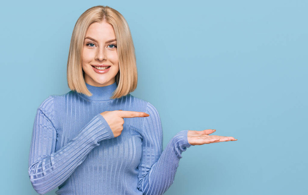 Young blonde woman wearing casual clothes amazed and smiling to the camera while presenting with hand and pointing with finger.  - Photo, Image