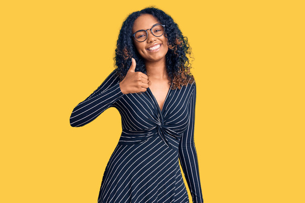 Young african american woman wearing casual clothes and glasses doing happy thumbs up gesture with hand. approving expression looking at the camera showing success.  - Photo, Image