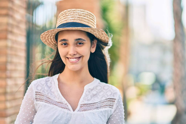 夏の帽子をかぶった若いヒスパニック系の観光客の女性が街に立って. - 写真・画像