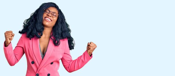 Прекрасна афро-американська жінка в діловій куртці і окулярах дуже щаслива і захоплена жестом переможця з піднятими руками, посміхаючись і кричачи про успіх. Святкування.  - Фото, зображення
